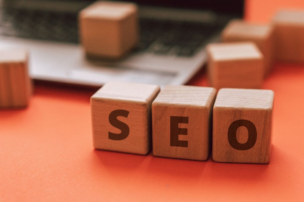 bloques de madera con letras SEO sobre un escritorio y junto a una laptop